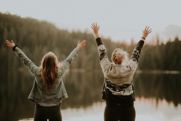 Two women raising their arms in celebration at a misty lakeside