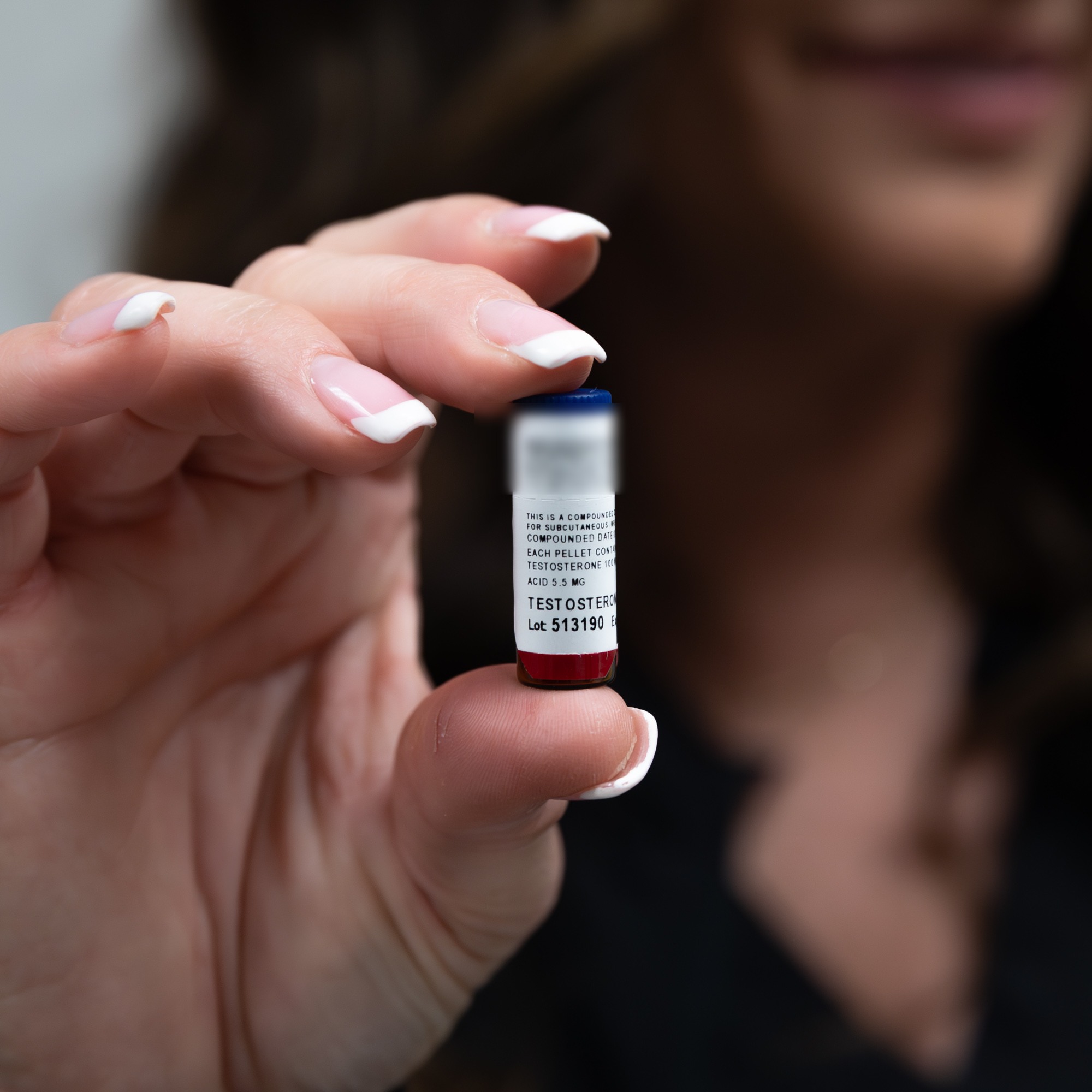 A compounded bioidentical hormone pellet vial, held between two fingers